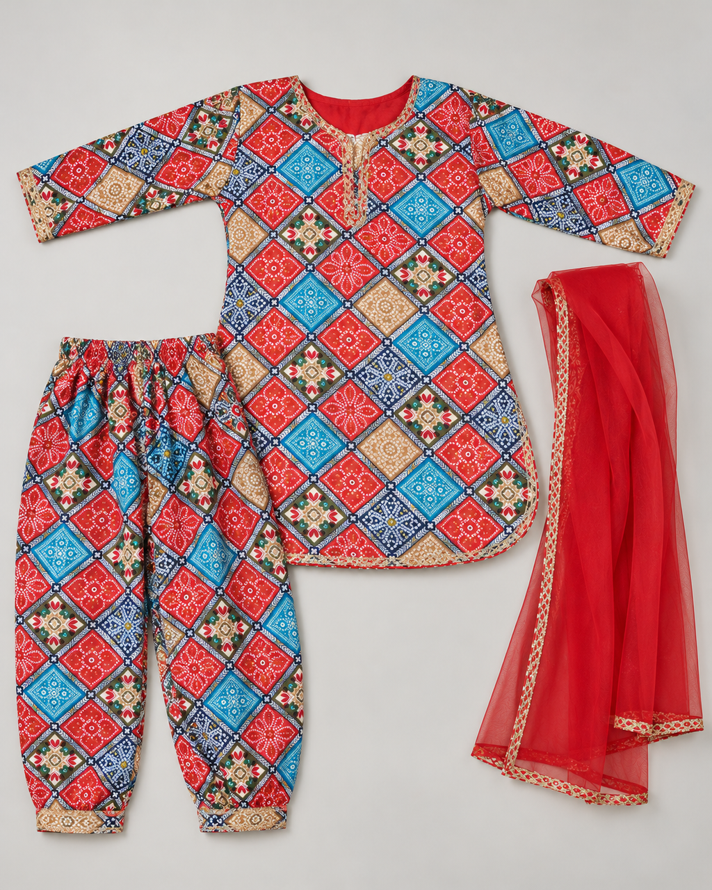 A children's traditional outfit set laid flat on a light gray background, featuring a long-sleeve tunic top, matching pants, and a sheer red dupatta. The fabric has a colorful geometric diamond pattern in red, blue, beige, and black, with a solid red inner lining and gold-toned decorative borders.