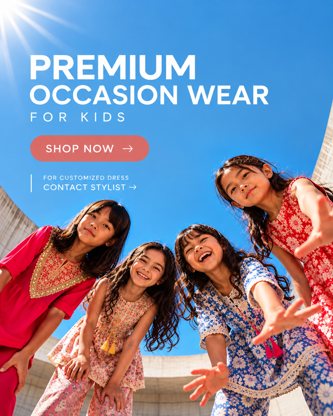 Promotional banner for kids' occasion wear featuring four young girls in colorful patterned traditional outfits looking up at the camera against a bright blue sky. Large white text reads 'PREMIUM OCCASION WEAR FOR KIDS' with a coral 'SHOP NOW' button.
